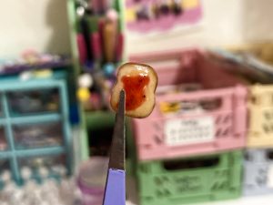 A tiny sculpted piece of toast with jam is being held with some tweezers