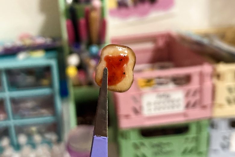 A tiny sculpted piece of toast with jam is being held with some tweezers